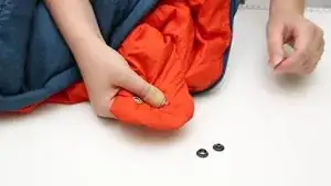 Anbringen eines neuen Druckknopfes 2. Seite: Füllung zur Seite schieben und Stoff zurecht schieben. Beide Teile des Druckknopfs einsetzen und mit Lochwerkzeug festdrücken und mit dem Hammer kräftig drauf schlagen.