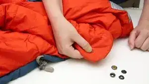 Anbringen eines neuen Druckknopfes: 1. Seite: Füllung zur Seite schieben und Stoff zurecht schieben. Beide Teile des Druckknopfs einsetzen und mit Lochwerkzeug festdrücken und mit dem Hammer kräftig darauf schlagen.